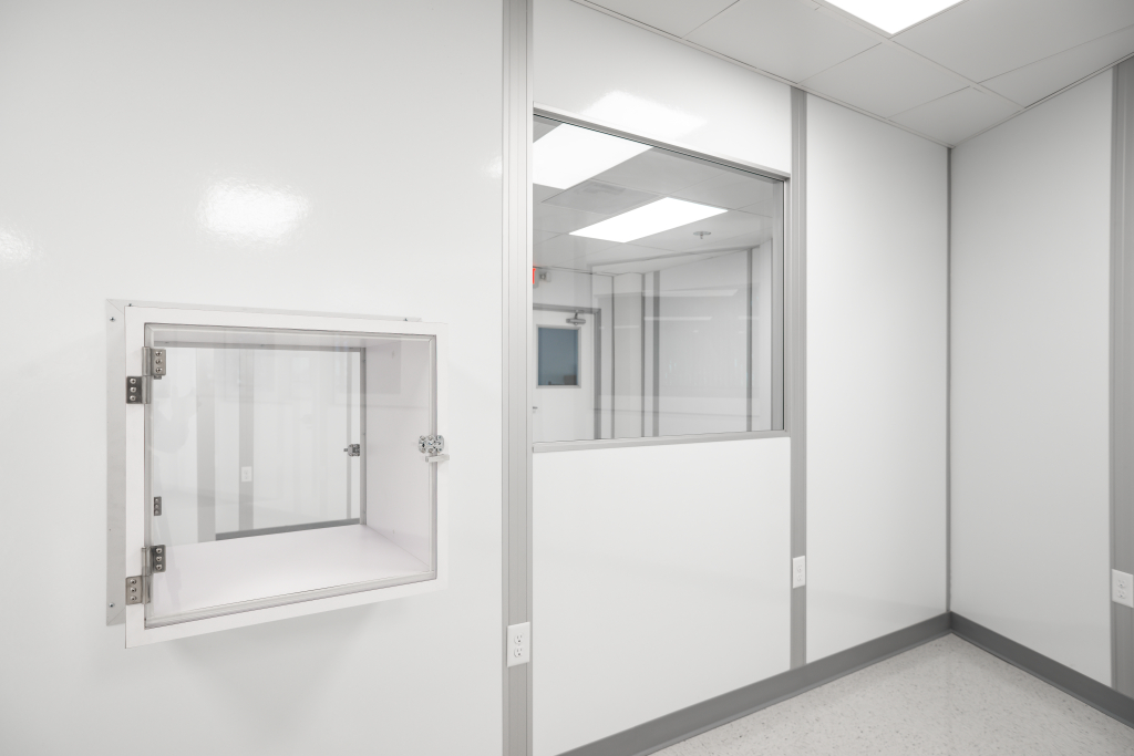 Cleanroom wall system featuring non-progressive panels with integrated windows and a pass-through chamber, designed for easy reconfiguration and maintaining a controlled environment