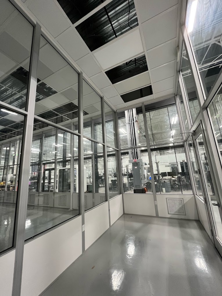 Cleanroom Walls: A Look at Materials and Systems Interior view of a cleanroom with glass walls and modular aluminum framing, showcasing visibility into the adjacent workspace.