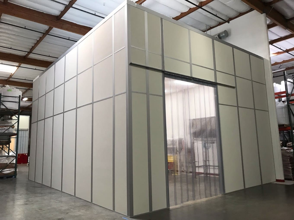 Clean Packaging Rooms: Everything You Need to Know A modular packaging room with a clean and organized structure, featuring a large entryway with transparent plastic strip curtains inside a warehouse.