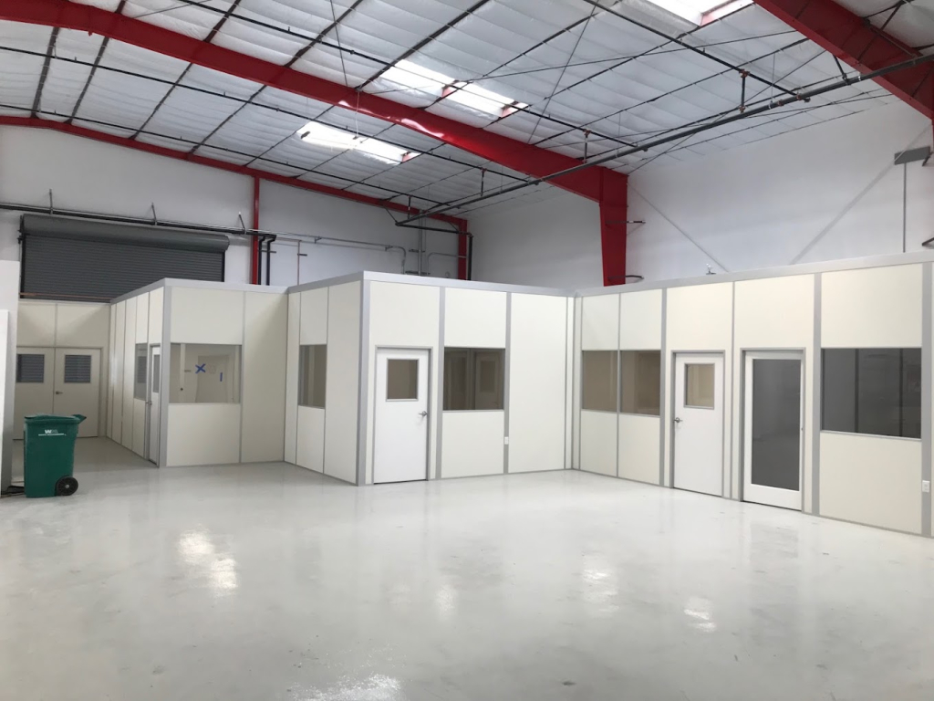Cleanroom Checklist: Steps to Successful Design A warehouse interior featuring modular cleanrooms with white walls, windows, and red ceiling beams.