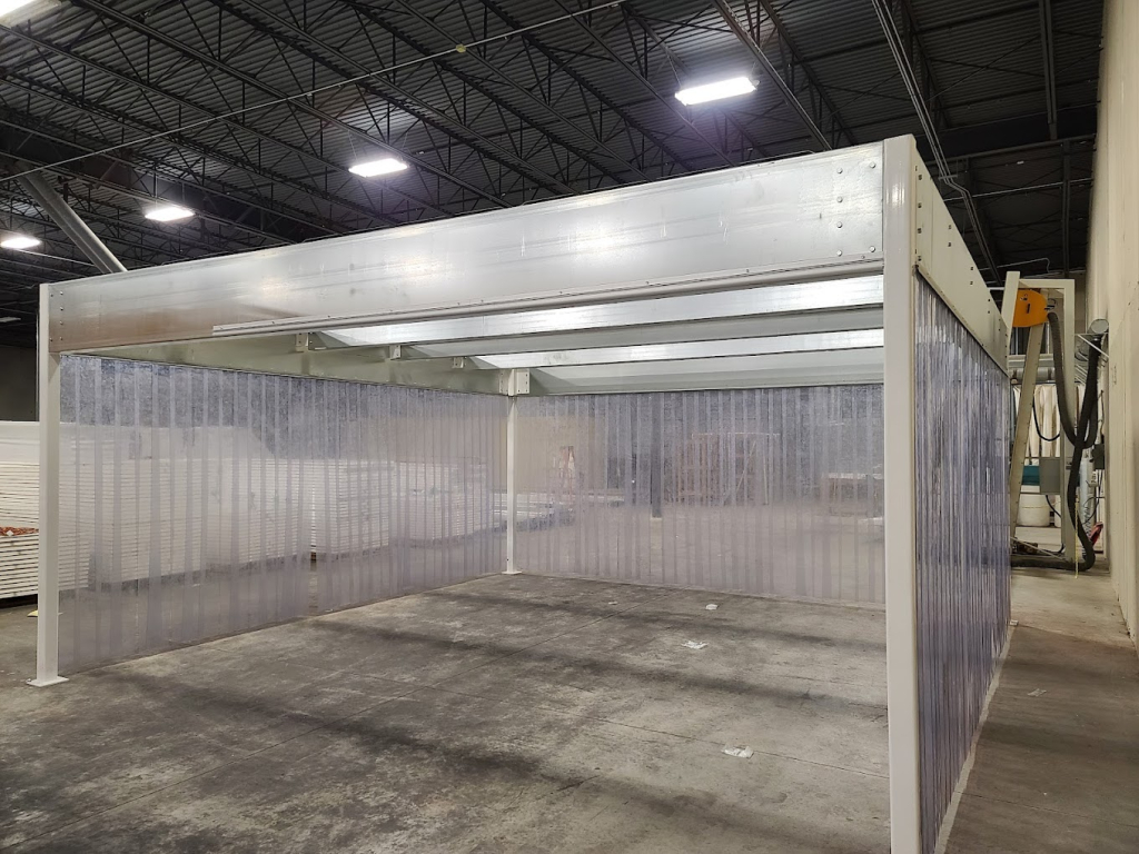 Softwall cleanroom with clear flexible walls and a sturdy overhead frame inside an industrial facility.