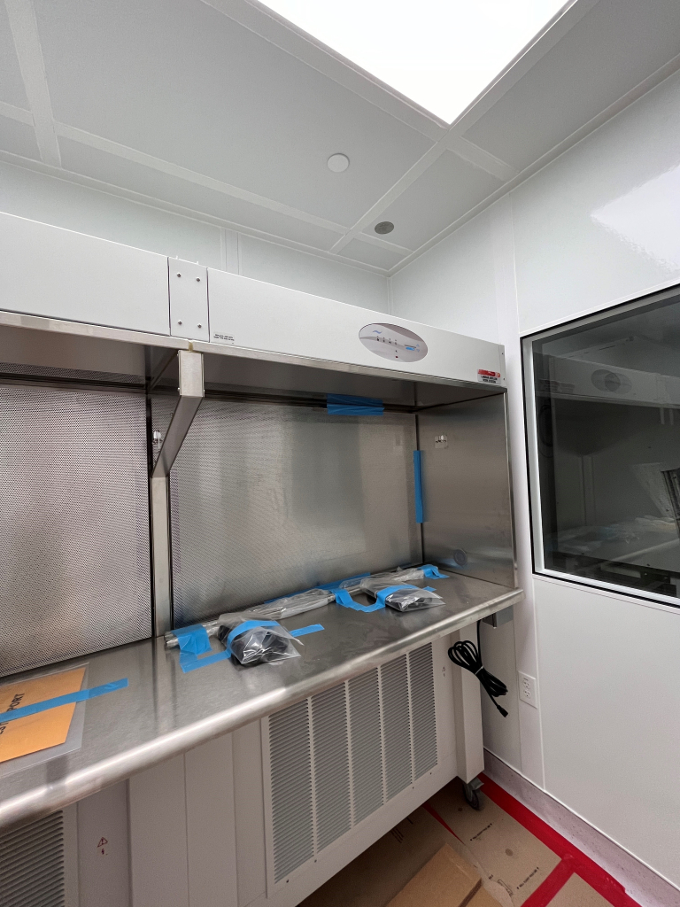 Horizontal vs Vertical Laminar Flow Hoods: A Simple Guide A horizontal laminar flow hood with a stainless steel work surface and a back-mounted HEPA filter, designed to provide a clean airflow across the workspace. The hood is installed in a cleanroom environment with visible taped components on the work surface for setup or maintenance.