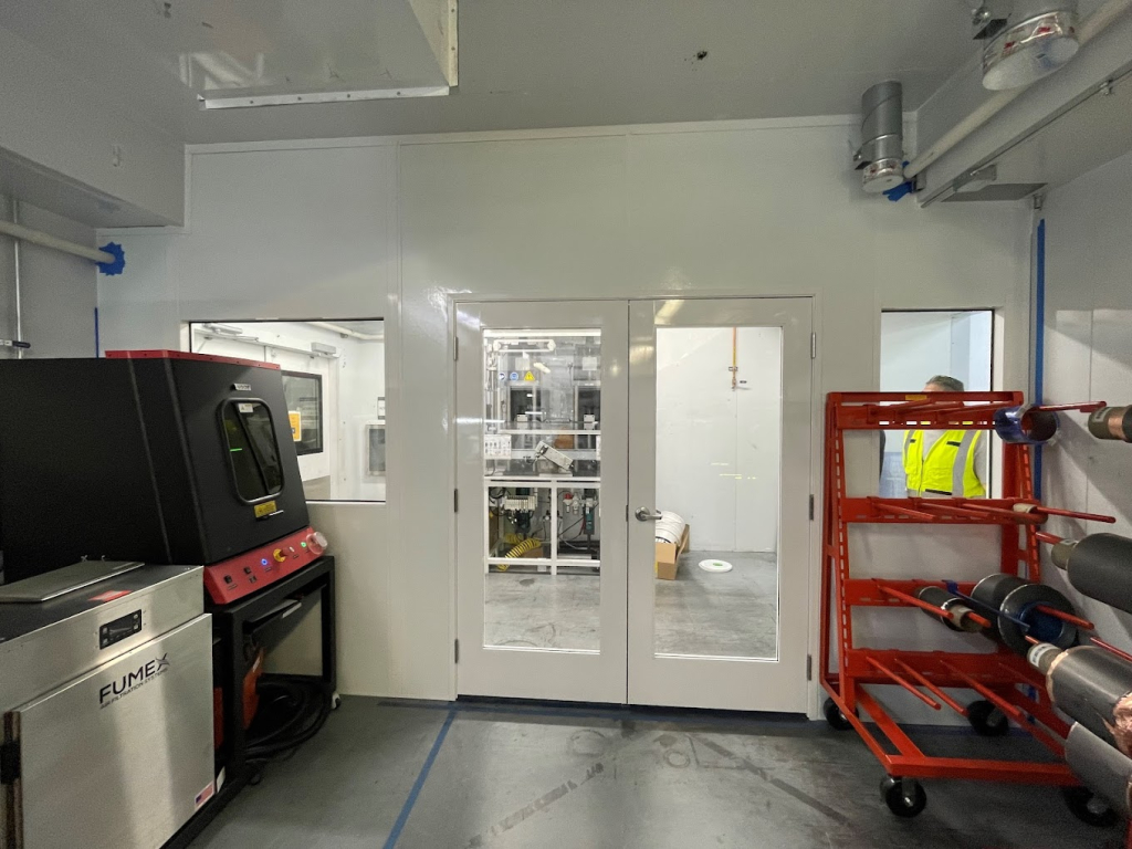 Electronics Cleanrooms 101: Everything You Need to Know Interior view of a modular cleanroom with observation windows, a Fumex filtration system, and storage racks holding spooled materials, designed for precise and controlled manufacturing processes.