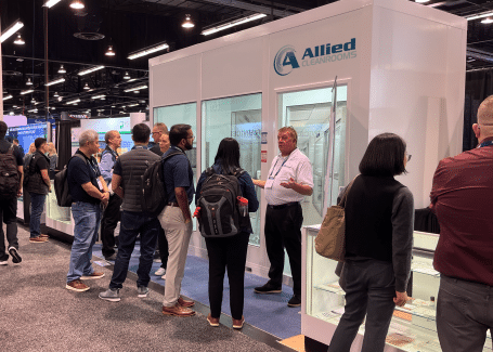 Attendees gather at the Allied Cleanrooms trade show booth, viewing a modular cleanroom structure and speaking with company representatives.