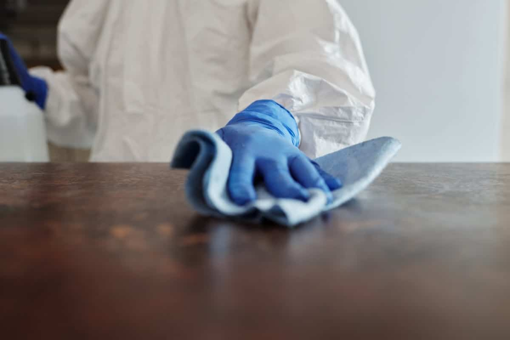 Cleanroom Wall Finishes: Cleaning, Sealing & Contamination Person in protective gear cleaning a surface with a disinfectant wipe, ensuring contamination control and hygiene